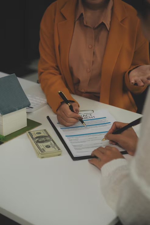 What is an escrow account - homeowner signing mortgage contract with cash and house model on desk
