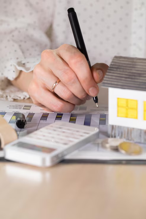 Woman calculating mortgage amortization schedule with calculator and house model