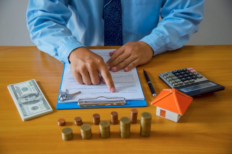 Mortgage closing costs paperwork with calculator, cash, coin stacks, and house model on desk