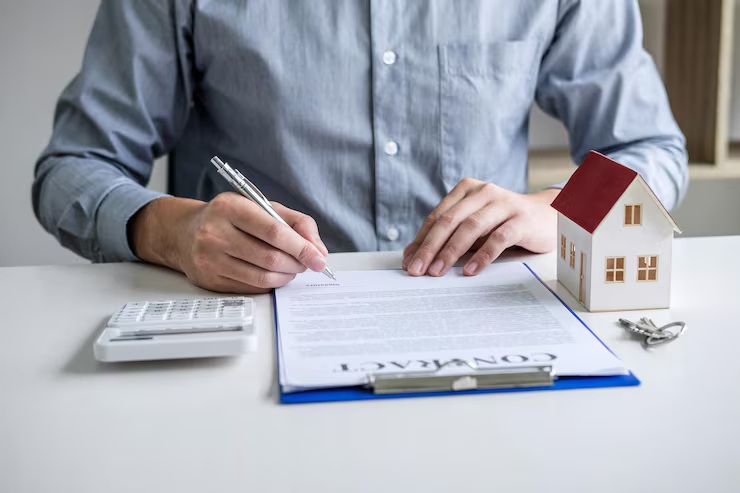 Mortgage underwriting approval — person signing contract with calculator, house model, and keys on desk