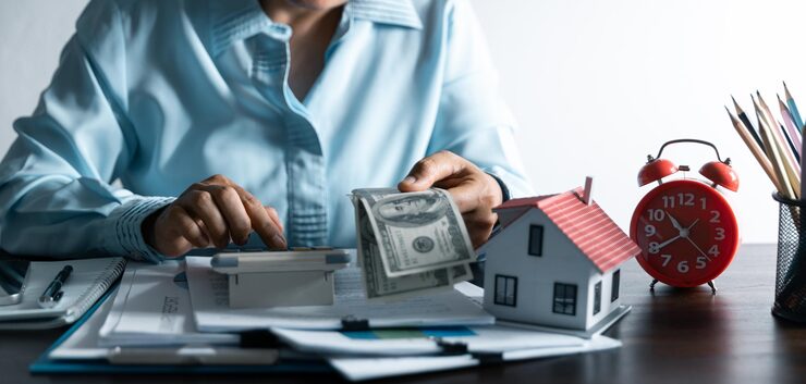 Person calculating whether to pay off mortgage early, holding cash next to a house model and calculator